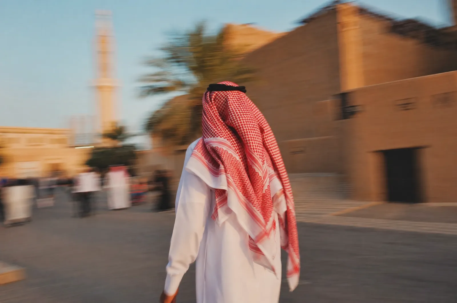 رجل سعودي بالثوب والشماغ يمشي بسرعة، صورة دافئة فيها حركة